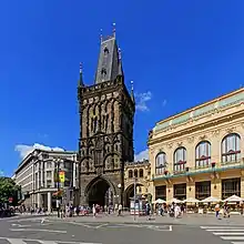 Une vue de la ville : à gauche, un bâtiment gris moderne ; au centre, une tour gothique, noire ; à droite, un bâtiment art nouveau, de couleur claire.