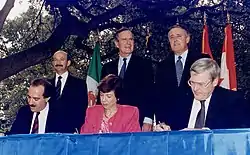 Photographie des premiers ministres du Canada, des États-Unis et du Mexique debout derrière les trois ministres du Commerce international de ces pays, signant l'Accord de libre-échange nord-américain.